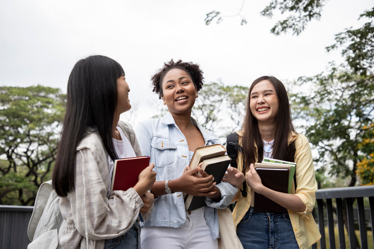 Diversity of happy woman student holding books and looking at natural outdoors at park. Prepare for college and university concept. Informal education and natural research