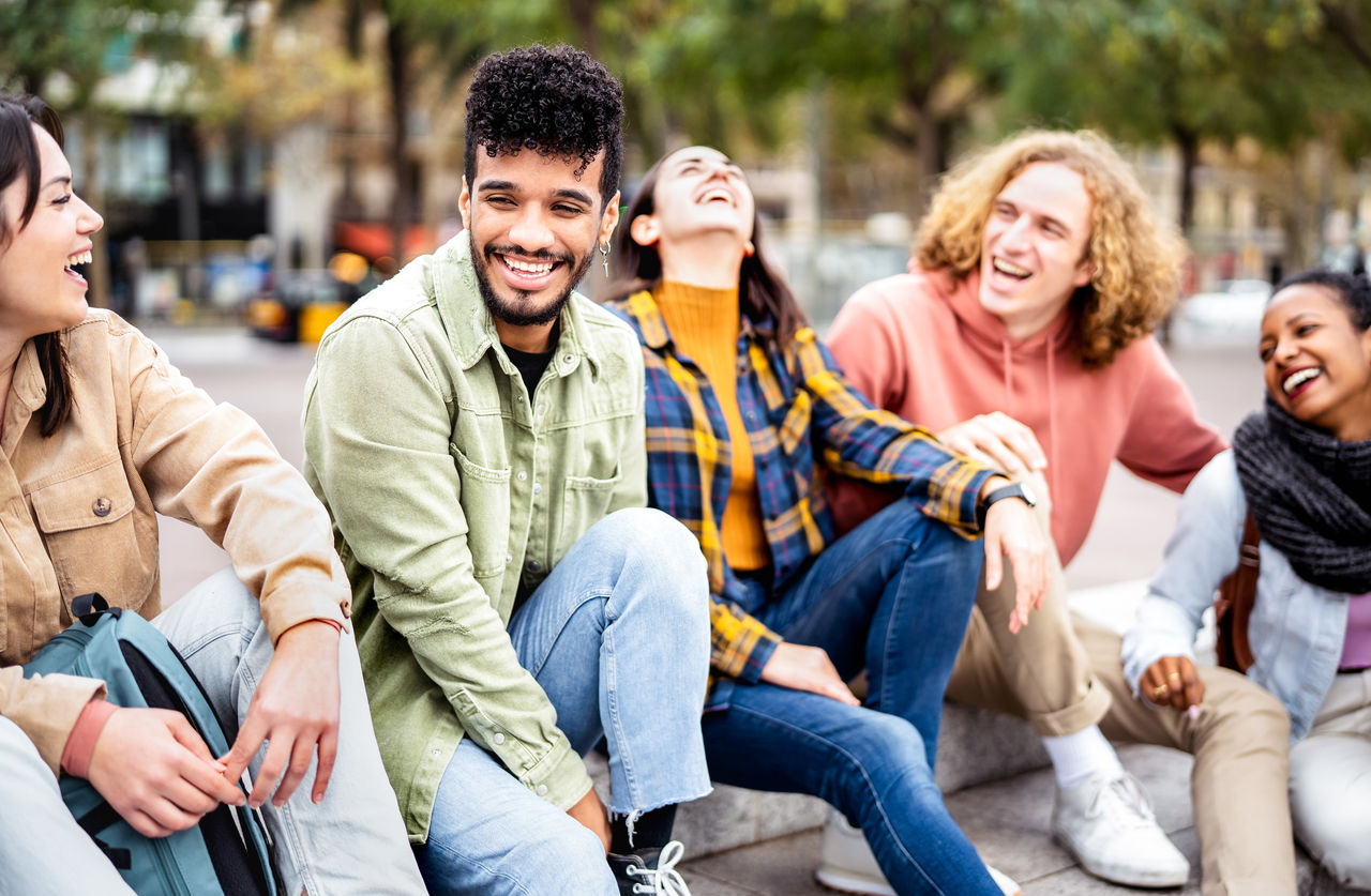 Milenial friends sitting together at city center on life style concept - Happy guys and girls having fun talking around Barcelona street - University students on travel vacation  - Bright vivid filter