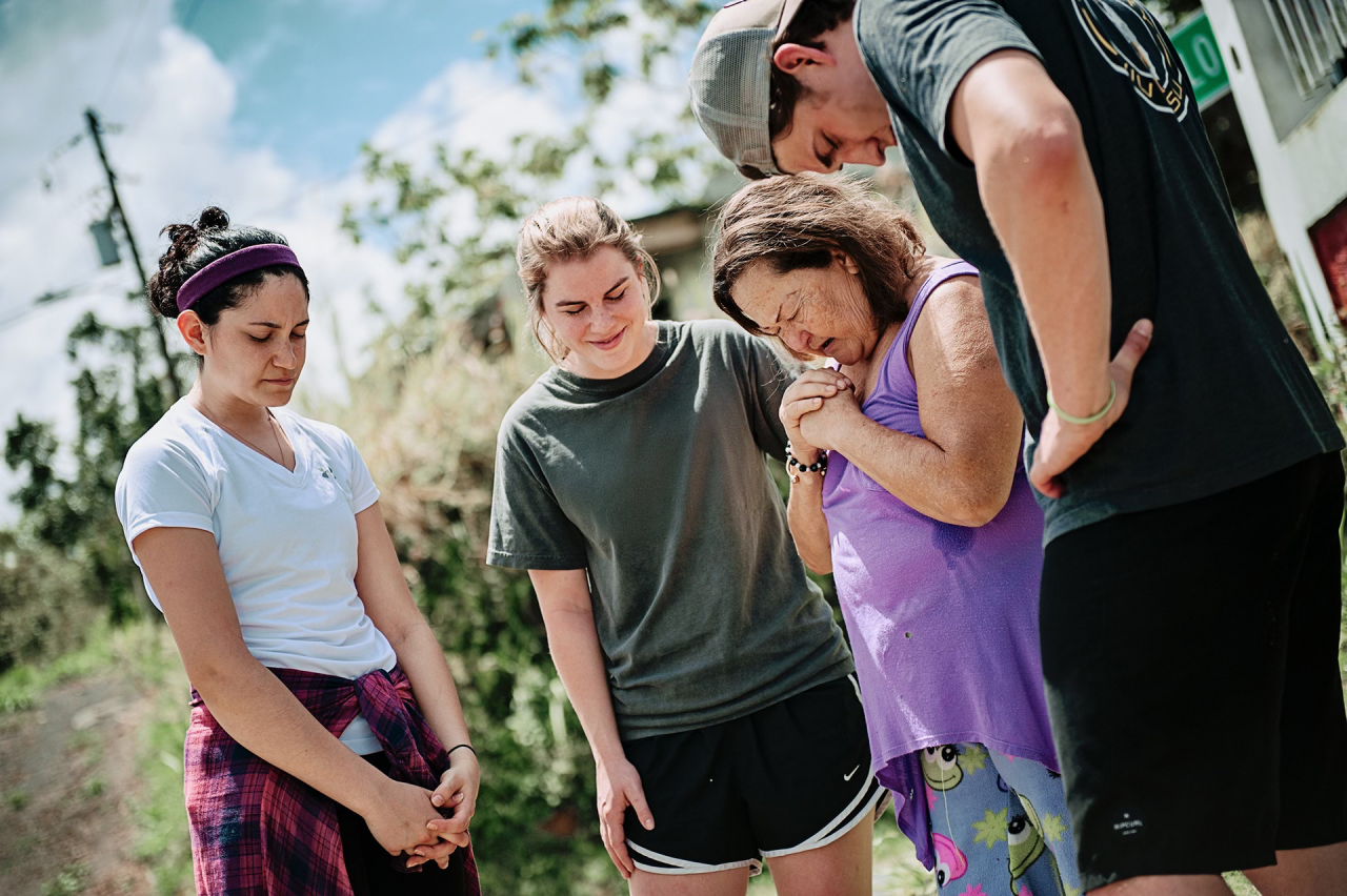 Group of people gathered in prayer outside field.